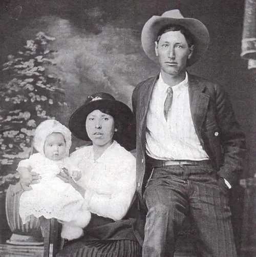 Studio posed monochrome family portrait. Man and woman in western wear. Woman holding child in gown. 