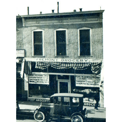 Green monochrome photo of a storefront for Fremont Grocery with a Model T era car parked in front.