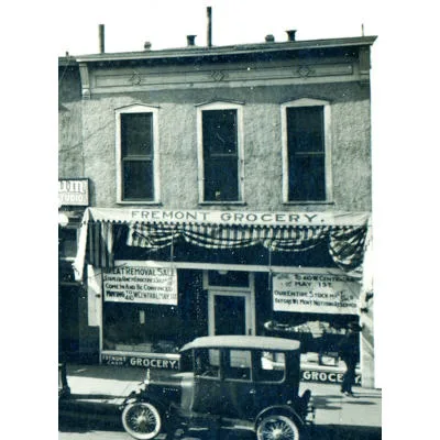 Green monochrome photo of a storefront for Fremont Grocery with a Model T era car parked in front.